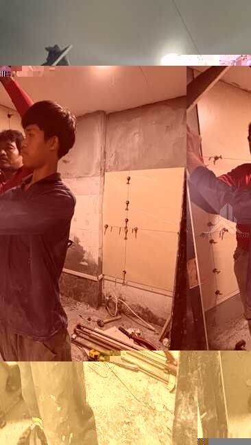 Two workers tiling a bathroom wall during a pattaya condo renovation, with tile-cutting tools on the floor