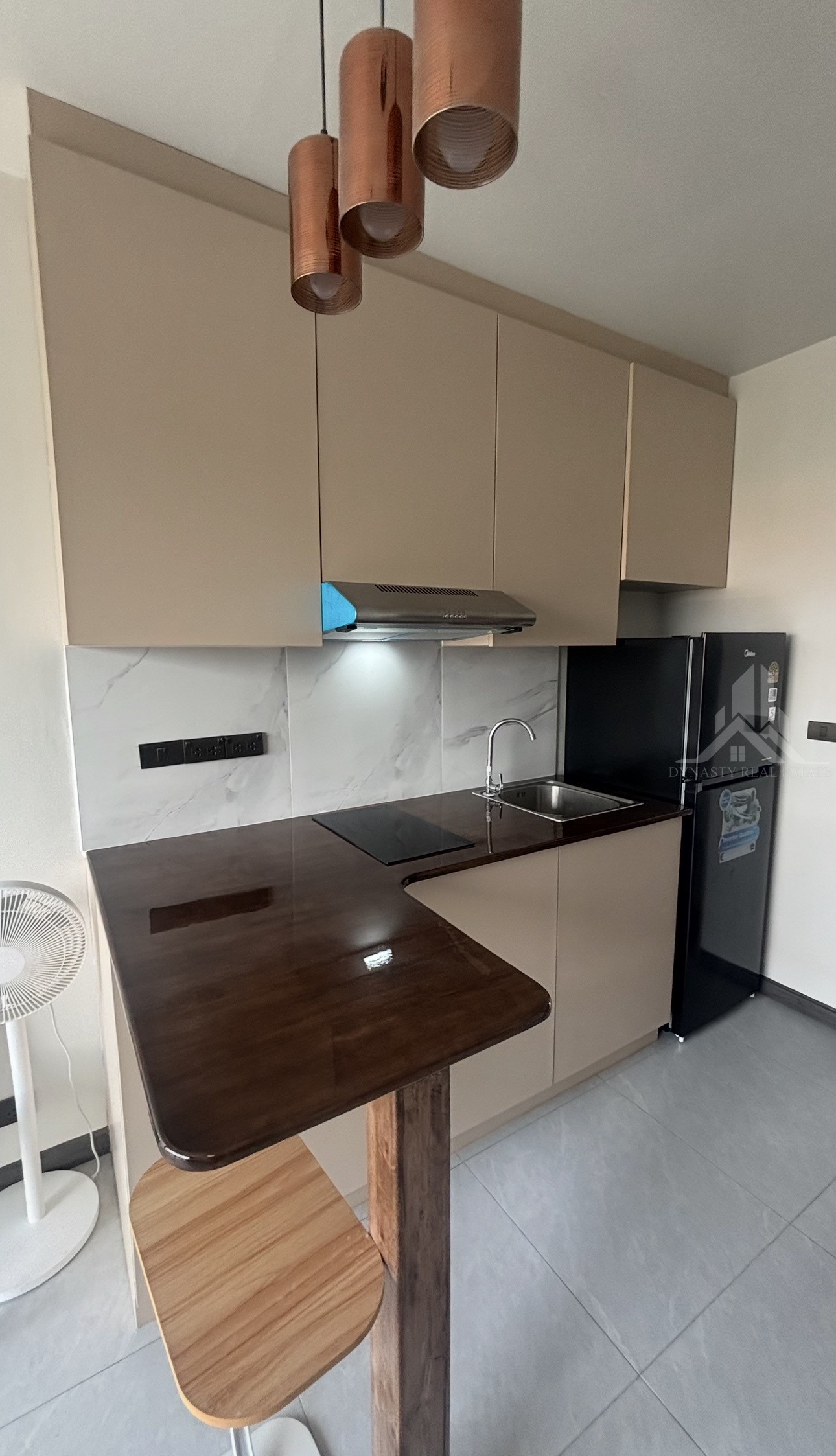 Completed: Built-In Furniture Renovation At Treetops Pattaya Condo For Sale In Pattaya L-shaped dark wood bar counter with copper pendant lights and beige kitchen cabinets in a treetops pattaya condo