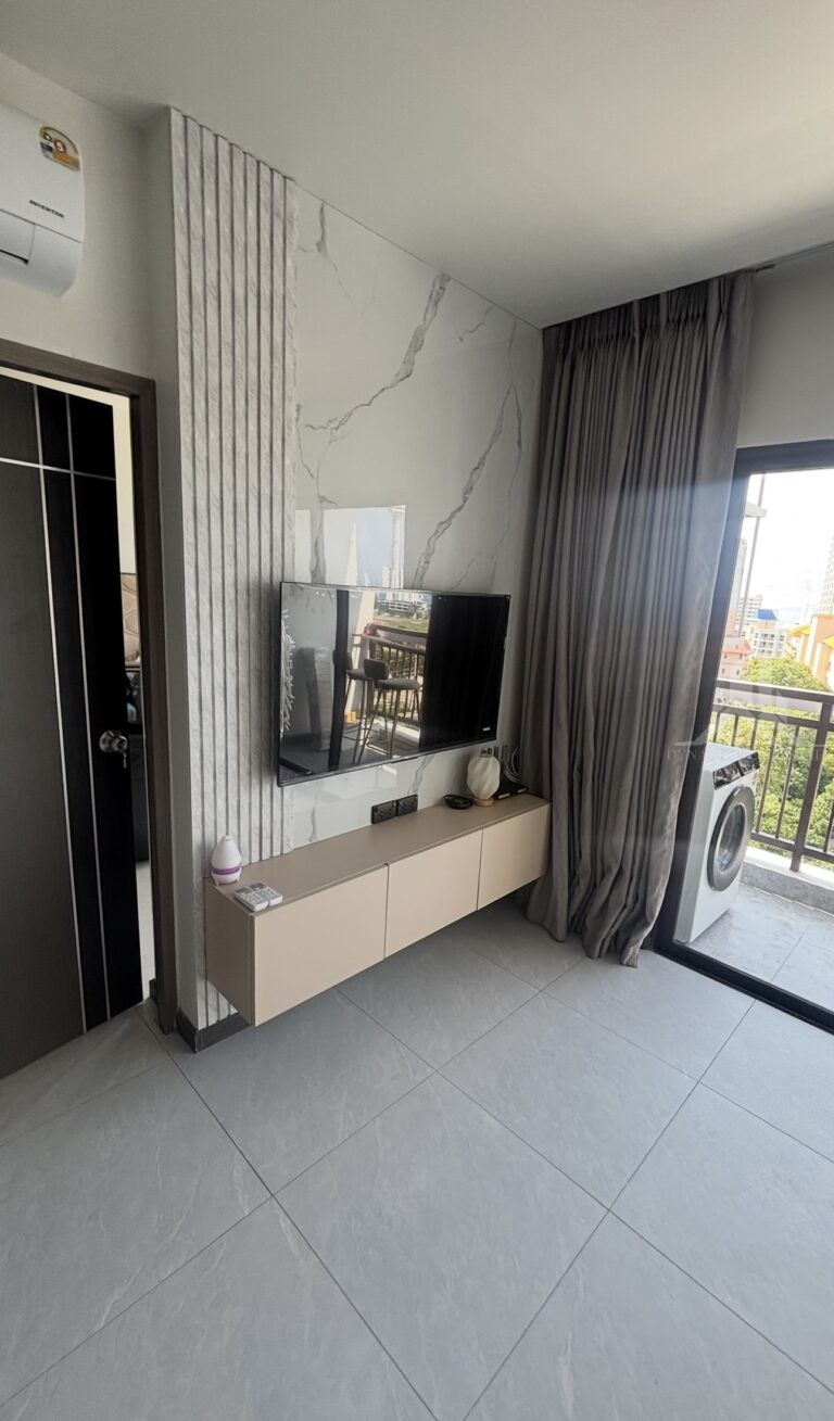 Treetops Pattaya condo living room with floating TV cabinet, marble-look feature wall and balcony view